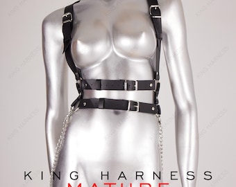 May include: Black leather harness with silver buckles and a chain detail. The harness has two straps that cross at the front and two straps that go around the waist.