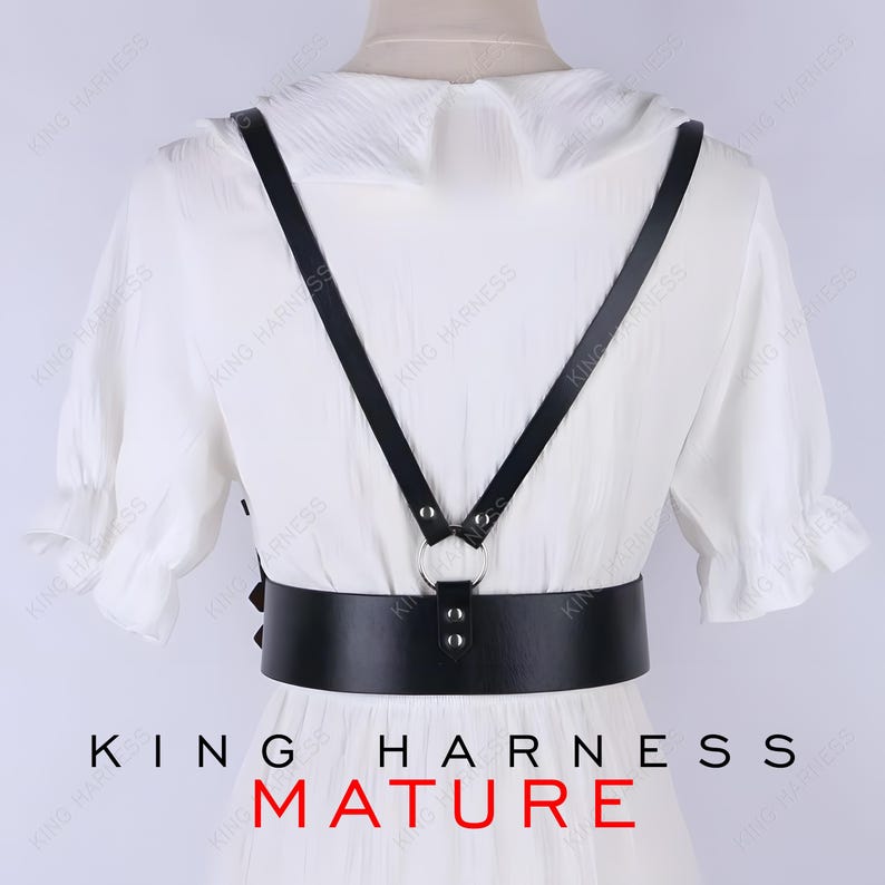 May include: Black leather harness with a wide belt and shoulder straps, connected by a silver ring. The harness is worn over a white dress. The text "KING HARNESS MATURE" is at the bottom.