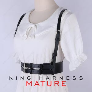 May include: Black leather harness with silver-tone buckles and straps. The harness features a double-belt design around the waist and shoulder straps. The text "KING HARNESS MATURE" is printed at the bottom of the image.