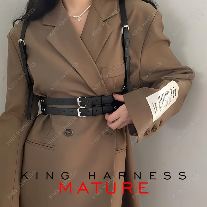 May include: Black leather harness with silver-tone buckles, worn over a brown blazer. The harness features two parallel belts around the waist and straps over the shoulders. The text "KING HARNESS" and "MATURE" are visible.