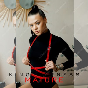 May include: A red leather harness with multiple straps and buckles. The harness is worn by a person with a black turtleneck shirt. The text "KING HARNESS MATURE" is visible in the image.