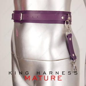 Puede incluir: Cintur&oacute;n de cuero morado con hebilla plateada y una correa de cuero morado a juego con un clip plateado. El texto "KING HARNESS MATURE" est&aacute; impreso debajo del cintur&oacute;n.