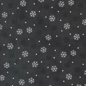 Op de afbeelding: Een donker antracietgrijze stof met een herhalend patroon van witte sneeuwvlokken in verschillende groottes, afgewisseld met kleine witte stippen die doen denken aan vallende sneeuw, wat zorgt voor een winterse textielprint.
