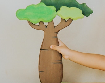 May include: A wooden tree toy with a brown trunk and green leaves. The tree is on a green base. The toy is designed for children and is made of wood.
