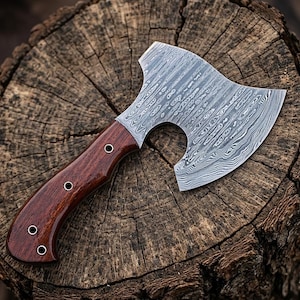 May include: A small, handcrafted axe with a patterned steel blade and a dark wood handle. The handle is secured with three rivets. The axe is resting on a weathered wooden surface.