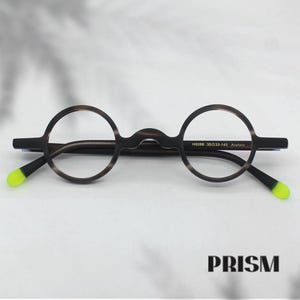 May include: Round spectacles with a brown and black speckled frame. The arms are dark brown with neon yellow tips. The text "H9266 35033-145 Acetate" is printed on the right arm. The word "PRISM" is printed at the bottom.