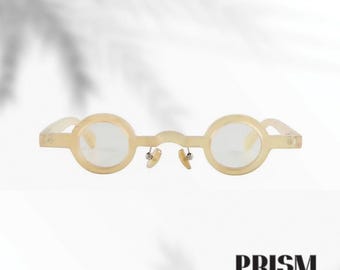Könnte beinhalten: Runde, hellfarbene Brille mit klaren Gläsern. Die Fassungen sind hellgelb und das Design umfasst kleine Nasenpads. Das Wort "PRISM" ist unten im Bild in Schwarz gedruckt.
