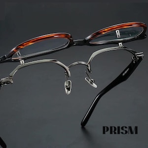 Puede incluir: Se muestran dos pares de gafas sobre un fondo oscuro. Un par presenta un patrón de carey en la montura superior y una montura inferior negra. El otro par tiene una montura de metal plateado con patillas negras. La palabra "PRISM" es visible.