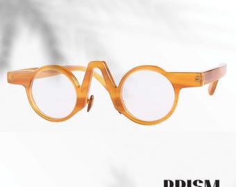 Könnte beinhalten: Orange getönte Brille mit runden Gläsern und einem einzigartigen Stegdesign. Die Fassungen haben eine hellbraune Farbe und der Markenname "PRISM" ist unten abgebildet. Die Brille hat einen Retro-Stil.