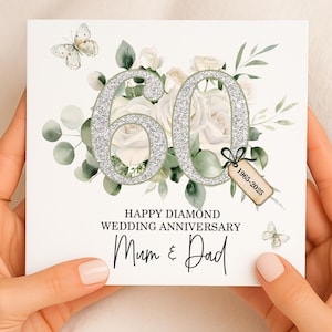 May include: A white square card with a floral design and the number 60 in silver glitter. The card reads "Happy Diamond Wedding Anniversary Mum & Dad" with butterflies and a tag that says "1965-2025".