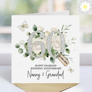 May include: A white 60th wedding anniversary card with silver glitter numbers, white roses, and green foliage. The card reads "Happy Diamond Wedding Anniversary" and "Nanny & Grandad". Includes a tag with the years 1965-2025.