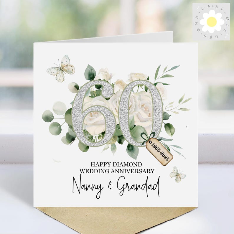 May include: A white 60th wedding anniversary card with silver glitter numbers, white roses, and green foliage. The card reads "Happy Diamond Wedding Anniversary" and "Nanny & Grandad". Includes a tag with the years 1965-2025.