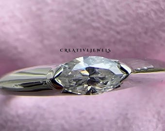 May include: A silver ring with a large, oval-shaped diamond set in a simple band. The ring is on a pink background.