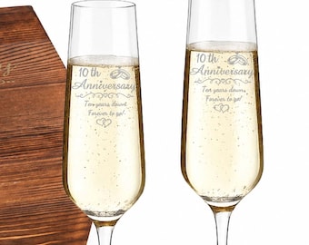 May include: A dark wood box with a metal latch, two clear glass champagne flutes, a silver heart-shaped bottle stopper, and a black corkscrew. The box and flutes are engraved with 10th Anniversary, Ten years down, Forever to go, and hearts.
