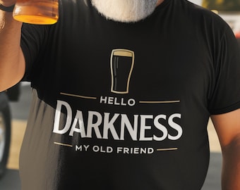 May include: Black t-shirt with the text "HELLO DARKNESS MY OLD FRIEND" in white and gold. The shirt features a beer glass graphic. A person is holding a glass of beer.