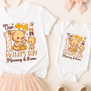 以下が含まれることがあります： ハチミツの入った瓶を持ったクマの可愛いデザインが施された白いTシャツ2枚。大きな方のTシャツには「Our Mothers Day Mommy & Liam」と書いてあり、小さい方のTシャツには「Our Mothers Day Mommy & Liam」と書いてあります。