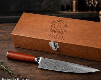 May include: A chef's knife with a reddish-brown wooden handle and a patterned metal blade, positioned in front of a rectangular wooden storage box. The box features a silver metal latch and an engraved crest with the letter S and the name SMITH.
