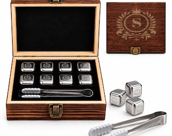 May include: A dark wood storage box with a brass latch containing eight silver-toned metal ice cubes, each engraved with the letter S, and a pair of metal tongs with white silicone tips. The box lid features a crown and wreath emblem with an S.