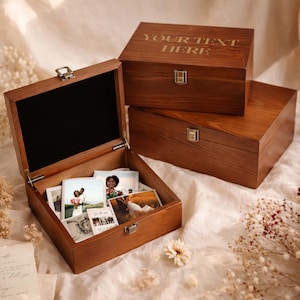 May include: Three wooden keepsake boxes with brass-colored clasps. The top box has the text "YOUR TEXT HERE" engraved on the lid. The open box contains photographs. The boxes are made of a warm-toned wood.