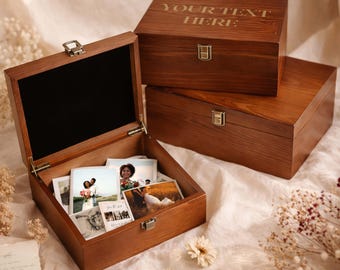May include: Three rectangular wooden keepsake boxes with a dark brown finish and metal latches. One box is open, revealing a black interior lining and several square photographs inside. The top box features the engraved text YOUR TEXT HERE.