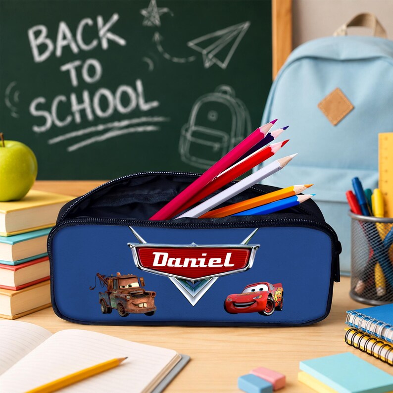 K&ouml;nnte beinhalten: Ein blaues, rechteckiges Federm&auml;ppchen mit den Disney Cars-Figuren Lightning McQueen und Hook sowie dem Namen Daniel in einem roten Emblem. Das M&auml;ppchen ist mit mehreren Buntstiften in den Farben Rot, Wei&szlig;, Gelb und Blau gef&uuml;llt.