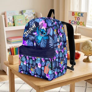 May include: A navy blue backpack featuring a Stitch character design. The backpack has a floral pattern with blue, purple, and white accents. The word "Stitch" is written in white. The backpack has black straps and a front pocket.