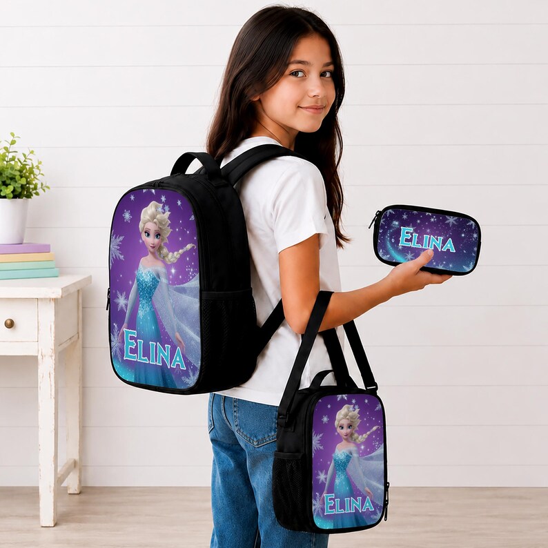 May include: A black backpack, a black lunch bag, and a black pencil case, each featuring a graphic of a blonde character in a blue dress against a purple snowflake background with the name ELINA printed in light blue letters on each item.