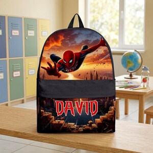 May include: A black backpack featuring a graphic print of Spider-Man in a dynamic pose against a sunset city skyline. The lower section displays the name DAVID in bold red letters with a white outline, set against a dark, textured brick background.