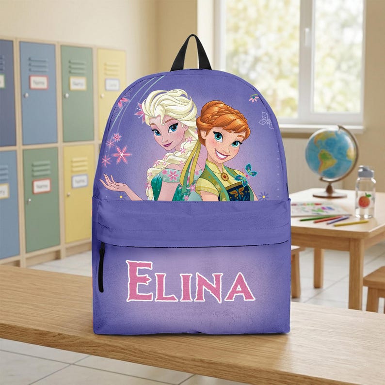 Op de afbeelding: Een paarse rugzak met een grafische print van twee geanimeerde personages met blond en kastanjebruin haar. Het voorvak toont de naam ELINA in grote witte hoofdletters. Het ontwerp bevat accenten van sneeuwvlokken en vlinders.