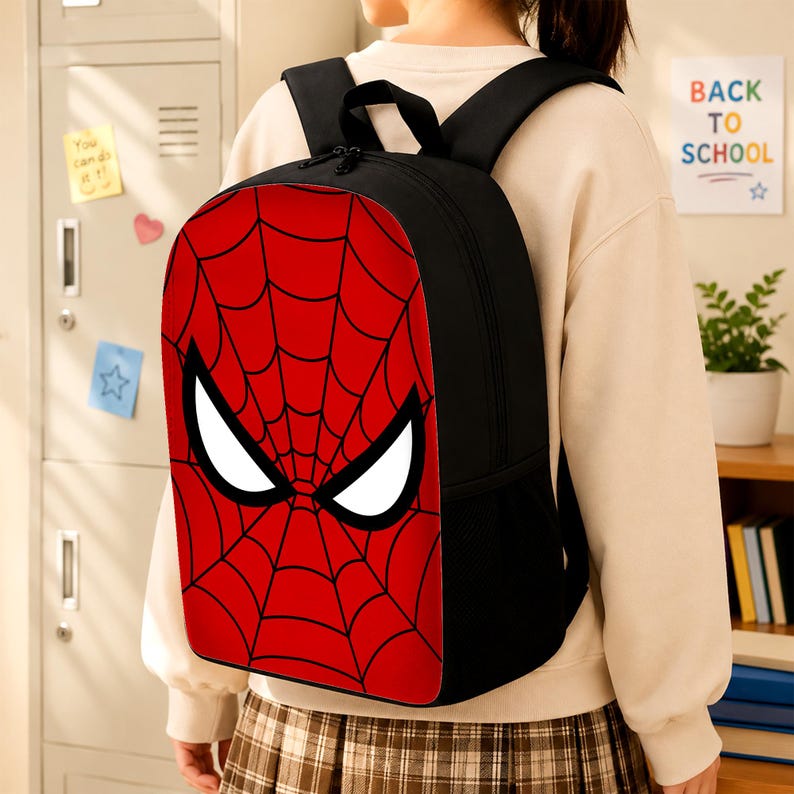 May include: A black backpack featuring a prominent red front panel with a black spiderweb pattern and two large white eye-shaped graphics. The bag includes black shoulder straps, a top handle, and side mesh pockets for storage and organization.