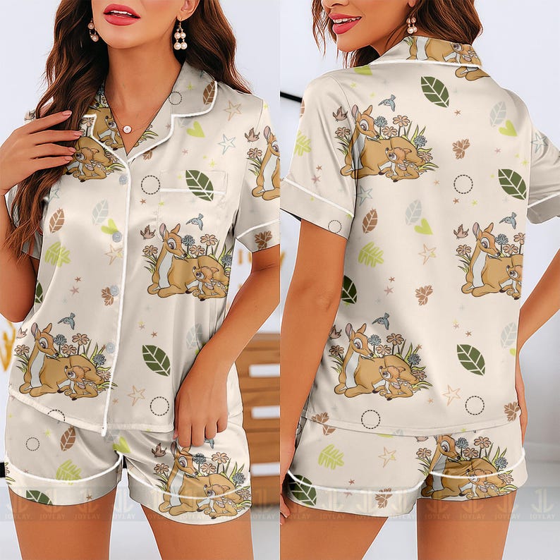 Op de afbeelding: Cr&egrave;mekleurige pyjamaset met een Bambi en Stampertje print. De top met korte mouwen en de shorts hebben witte biezen en knoopsluitingen. De set bevat een herhalend patroon van herten, bloemen, bladeren en vogels.