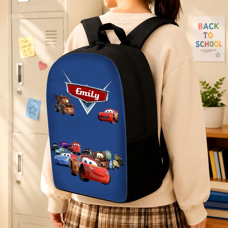 May include: A black backpack featuring a blue front panel with a graphic print of various animated car characters. A red emblem at the top displays the name Emily in white text. The bag includes black shoulder straps and side mesh pockets.