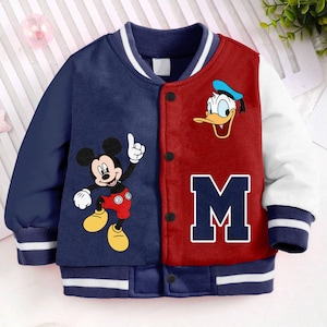 May include: A blue and red baseball jacket with a white stripe on the collar and cuffs. The jacket features a Mickey Mouse and Donald Duck design on the front. The letter "M" is printed on the red side of the jacket.