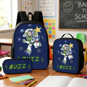 May include: A dark blue backpack, lunch bag, and pencil case set featuring a graphic of Buzz Lightyear in a white, green, and purple space suit. The design includes yellow stars, blue lightning bolts, and the text BUZZ in green lettering.
