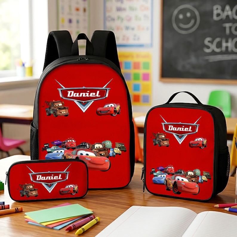 May include: A red backpack, lunch bag, and pencil case set featuring the Cars movie characters and the name Daniel printed in a silver emblem. Each item has black trim, black straps, and a graphic print of various colourful race cars.