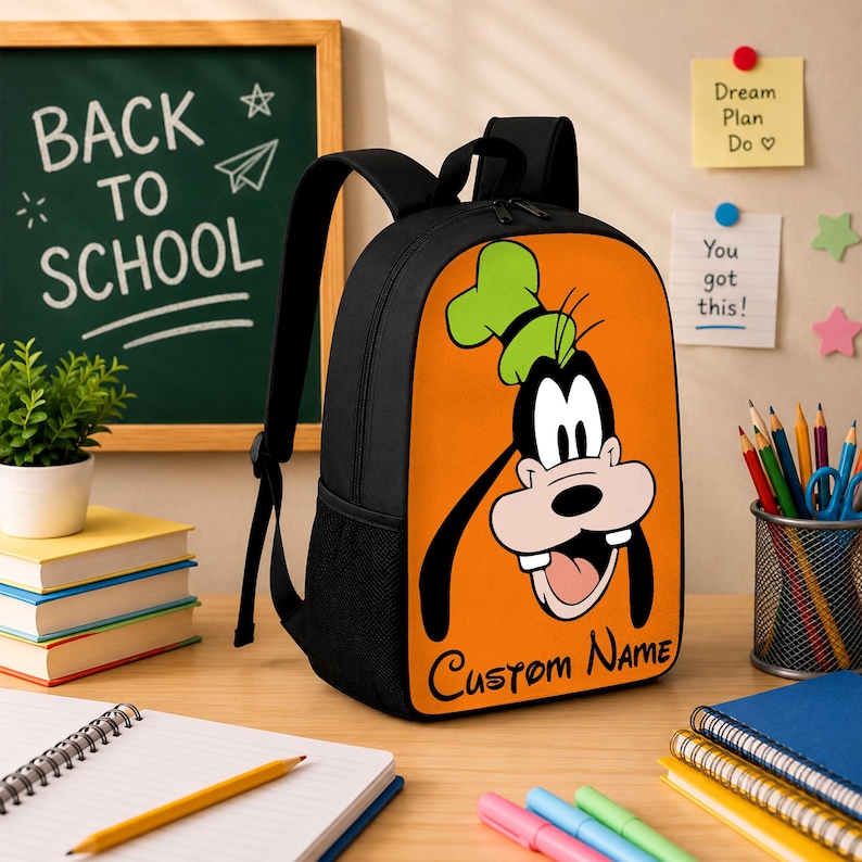 Peut inclure: Un sac &agrave; dos noir avec un panneau avant orange orn&eacute; d'une illustration du personnage de dessin anim&eacute; Dingo portant un chapeau vert. Le texte "Custom Name" est imprim&eacute; en &eacute;criture noire en bas du panneau orange. Le sac poss&egrave;de des bretelles noires.