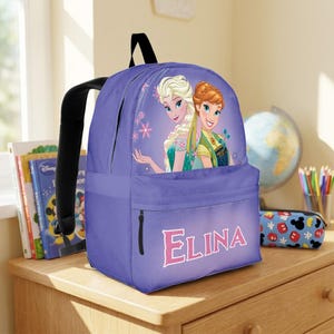 May include: A purple backpack featuring a graphic of Elsa and Anna from Frozen on the front pocket. The name ELINA is printed in large pink letters below the characters. The bag has black shoulder straps and a zippered main compartment.