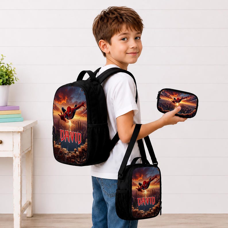 May include: A black backpack, a matching lunch bag, and a small pencil case, all featuring a graphic print of Spider-Man flying over a city at sunset with the name DAVID printed in red letters on the front of the backpack and lunch bag.