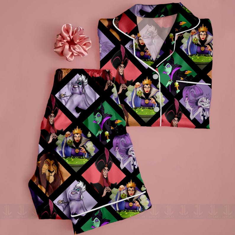 May include: A pajama set featuring a colorful pattern of Disney villains. The set includes a button-down top and matching pants, trimmed with white piping. A pink scrunchie is placed near the set on a pink background. The pajama set is made of a silky material.