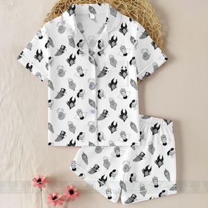 K&ouml;nnte beinhalten: Wei&szlig;es Pyjama-Set mit einem sich wiederholenden Muster von Cartoon-B&ouml;sewicht-Gesichtern in Schwarz und Grau. Das Set enth&auml;lt ein kurz&auml;rmeliges Button-up-Shirt und passende Shorts. Das Shirt hat wei&szlig;e Paspeln.