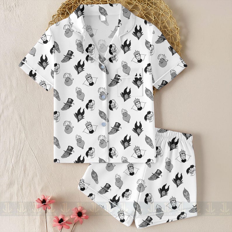 K&ouml;nnte beinhalten: Wei&szlig;es Pyjama-Set mit einem sich wiederholenden Muster von Cartoon-B&ouml;sewicht-Gesichtern in Schwarz und Grau. Das Set enth&auml;lt ein kurz&auml;rmeliges Button-up-Shirt und passende Shorts. Das Shirt hat wei&szlig;e Paspeln.