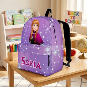 Pu&ograve; includere: Uno zaino viola con la grafica di un personaggio dai capelli intrecciati, motivi a fiocchi di neve bianchi ed effetti di luce scintillanti. La tasca frontale mostra il nome Sofia in grandi lettere rosa con contorno bianco e nero.