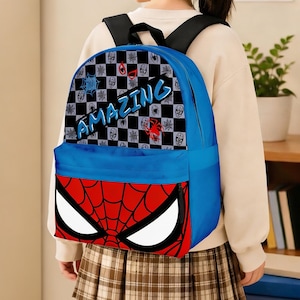 May include: Blue backpack featuring a Spiderman design. The front flap showcases Spiderman's mask, while the top section has a checkerboard pattern with spider emblems and the word "AMAZING". Black shoulder straps.