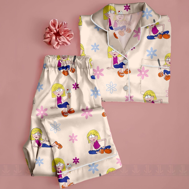 Pu&ograve; includere: Set pigiama color crema con stampa di personaggi dei cartoni animati e dettagli floreali rosa e blu. Il set include una camicia con bottoni e pantaloni abbinati. Un elastico rosa &egrave; posto vicino al pigiama.