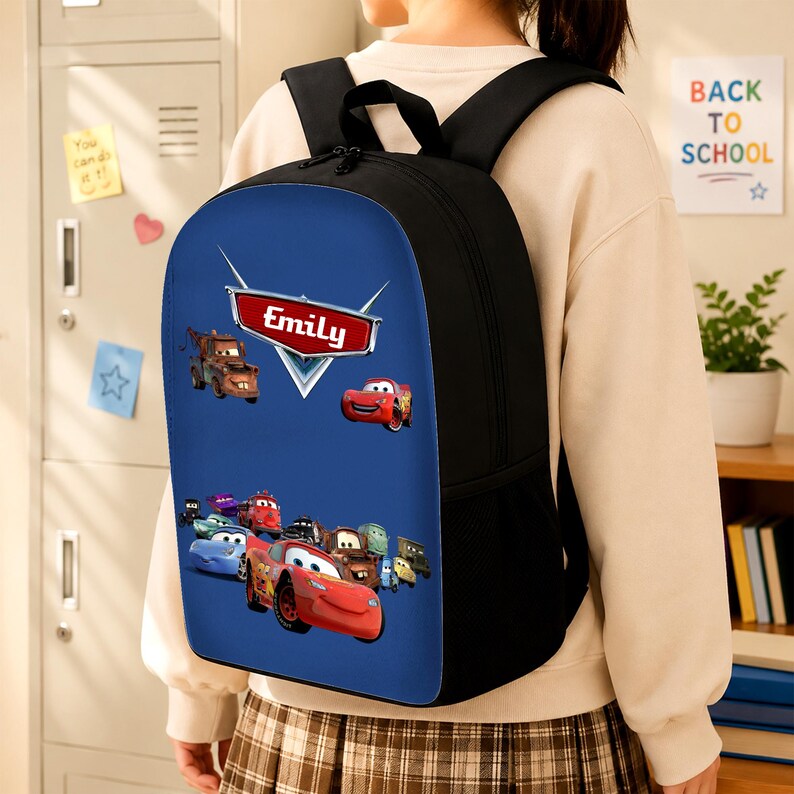 K&ouml;nnte beinhalten: Ein schwarzer Rucksack mit einer blauen Vorderseite, die mit verschiedenen animierten Auto-Charakteren bedruckt ist. Ein rotes Emblem oben zeigt den Namen Emily in wei&szlig;er Schrift. Der Rucksack hat schwarze Schultergurte und seitliche Netztaschen.