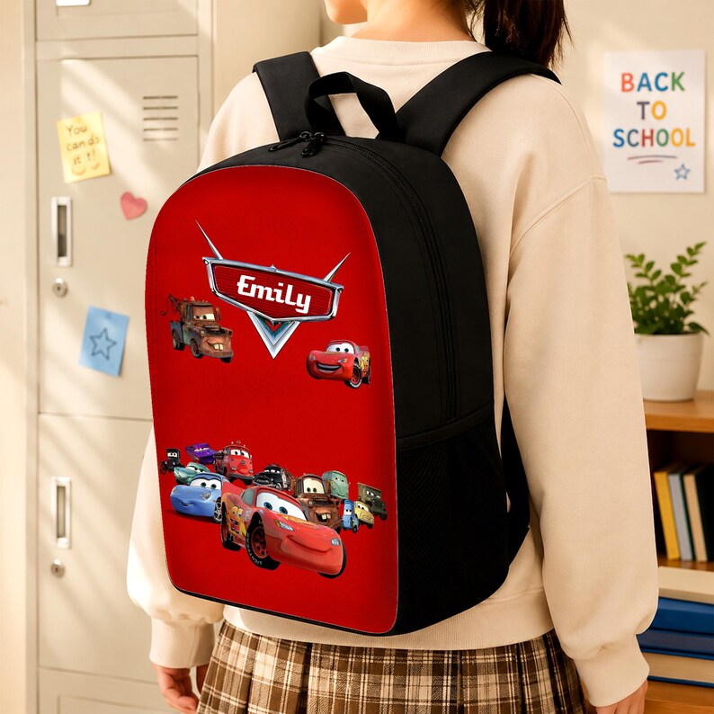 May include: A black backpack with a vibrant red front panel featuring a graphic print of various animated car characters. The design includes a central silver emblem with the name Emily printed in white text, along with multiple colourful vehicles.