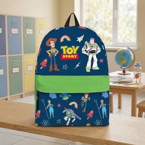May include: A navy blue backpack featuring characters from the animated film "Toy Story." The backpack has a green band across the middle and a black handle. The design includes Woody, Buzz Lightyear, and the words "Toy Story."