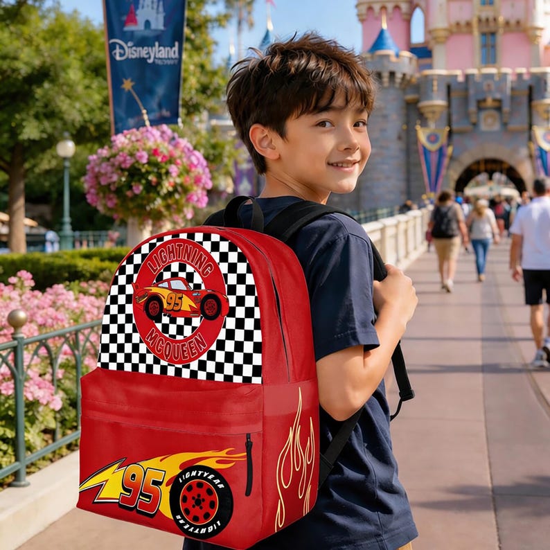 May include: Red backpack featuring Lightning McQueen from the Cars movie. The backpack has a black and white checkered pattern, the number 95, and flames. The backpack is being worn by a person in front of a castle.