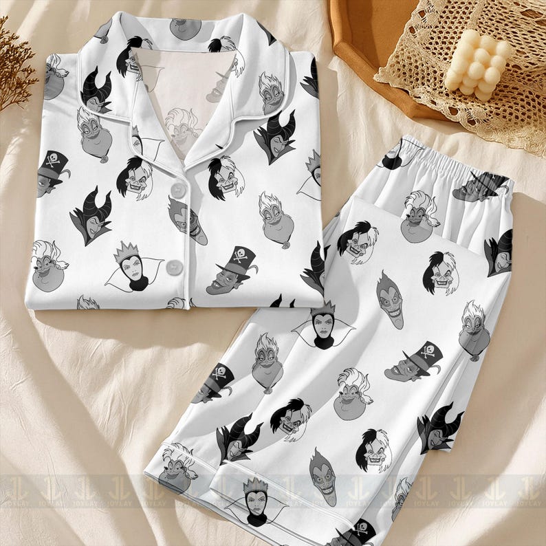 K&ouml;nnte beinhalten: Wei&szlig;es Pyjama-Set mit einem sich wiederholenden Muster von Cartoon-B&ouml;sewicht-Gesichtern in Graut&ouml;nen. Das Set beinhaltet ein Oberteil zum Kn&ouml;pfen und eine passende Hose. Der Pyjama ist aus einem weichen, bequemen Material gefertigt.