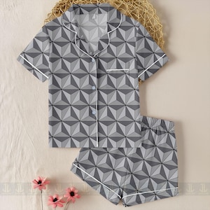 May include: A gray geometric patterned pajama set. The short-sleeved top has a button-down front and a chest pocket. The shorts have an elastic waistband. Both pieces are trimmed with white piping.